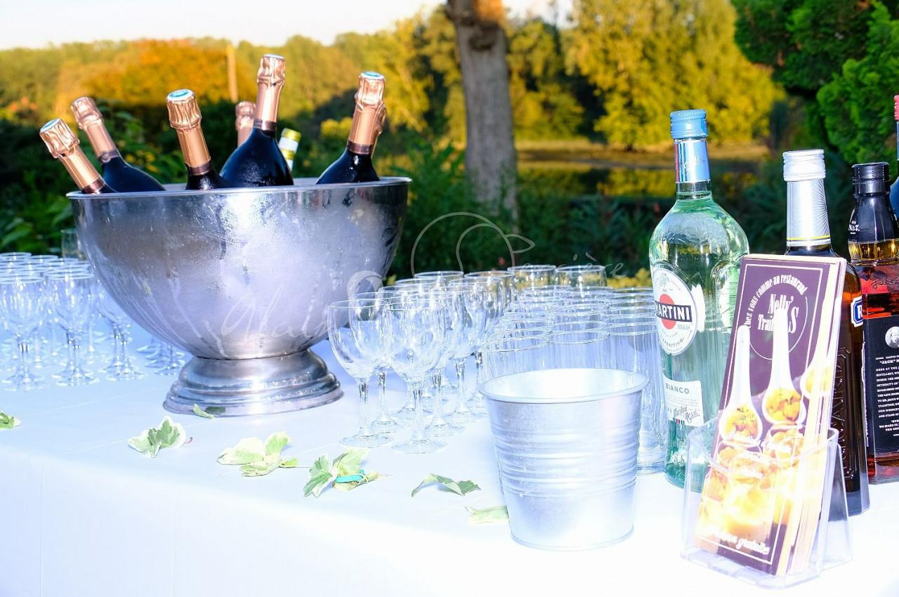 Table dressée en extérieur avec seau de champagne, verres, bouteilles d'alcool et décorations végétales.