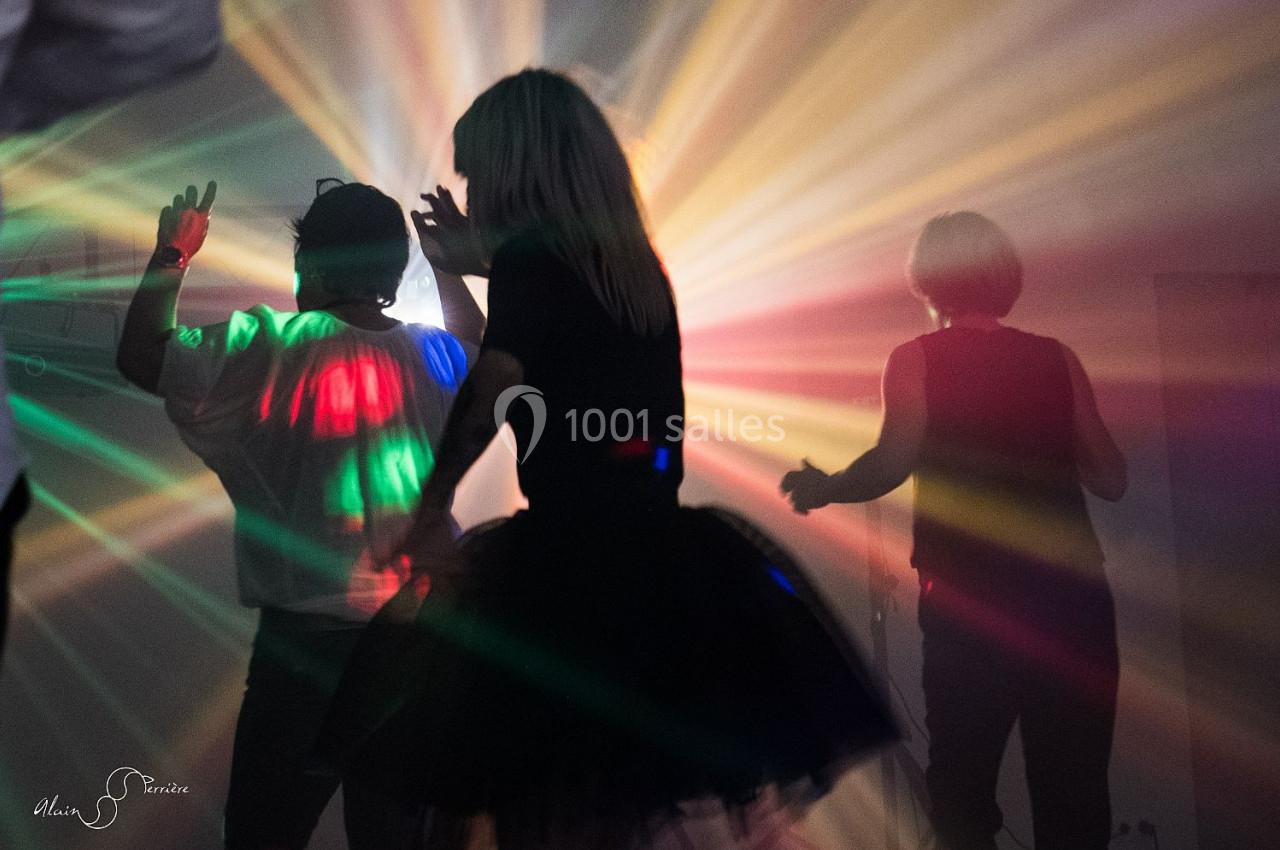 Personnes dansant dans une ambiance sombre avec des faisceaux lumineux colorés traversant la pièce.