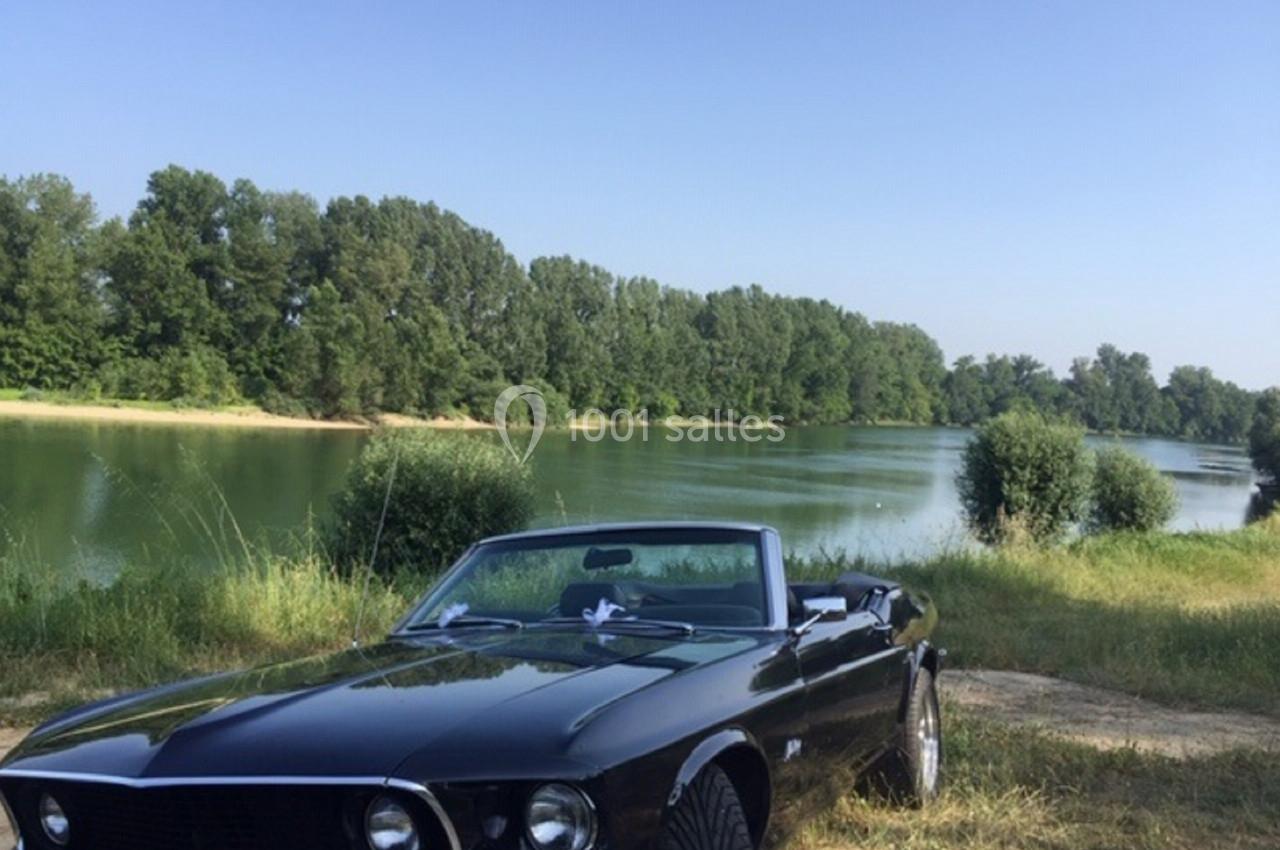 Voiture décapotable noire garée près d'un lac entouré de végétation et d'arbres sous un ciel dégagé.