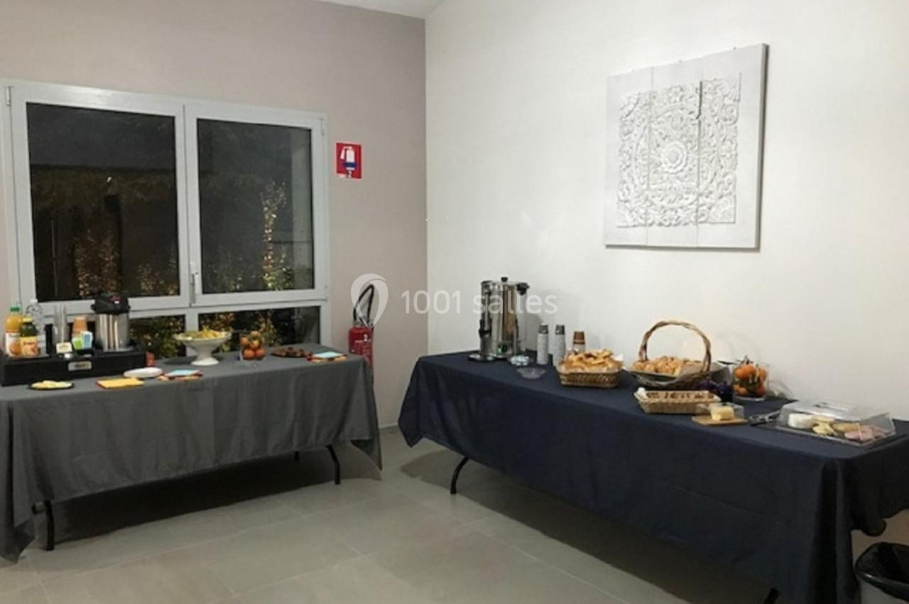 Buffet avec boissons, viennoiseries, fruits et condiments disposés sur deux tables dans une salle lumineuse.