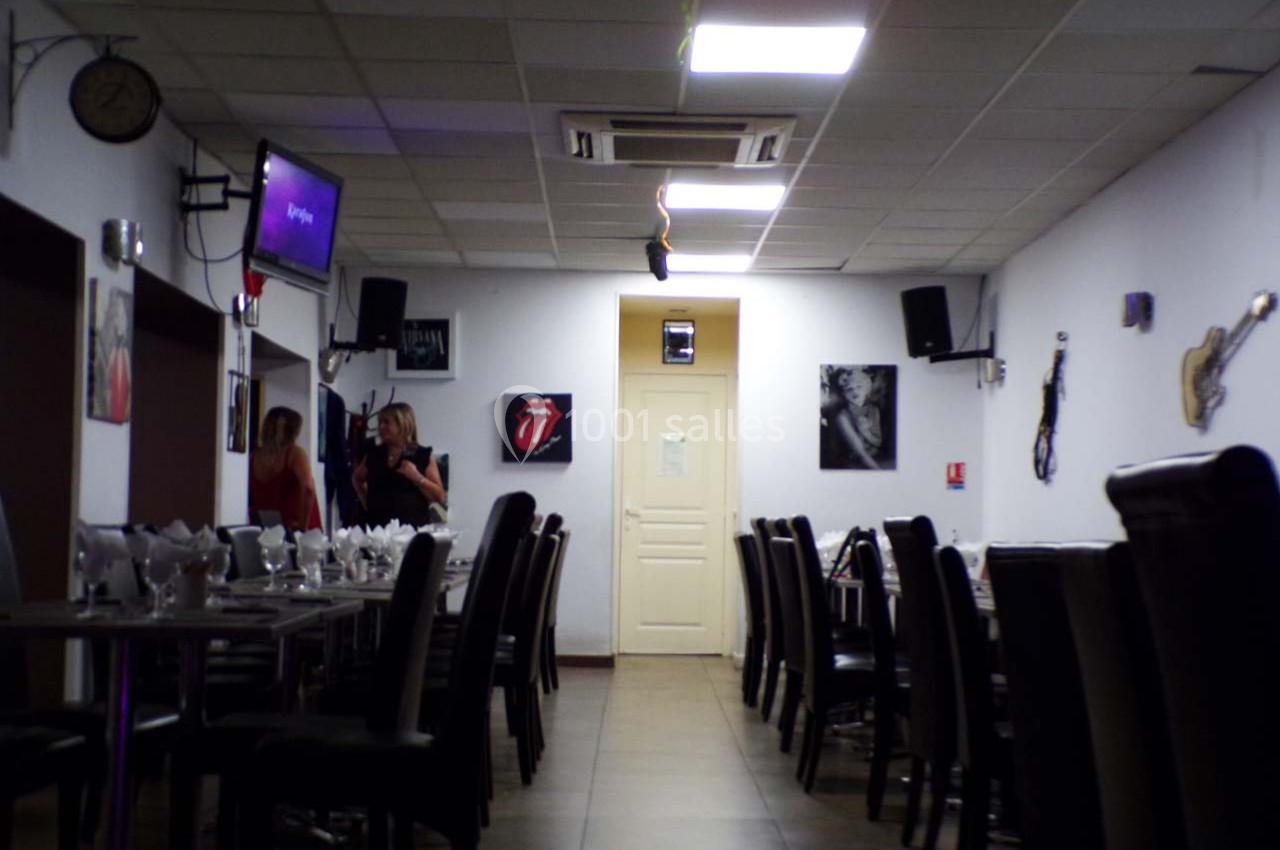 Salle de restaurant avec tables dressées, chaises noires, décorations murales et deux personnes discutant au fond.