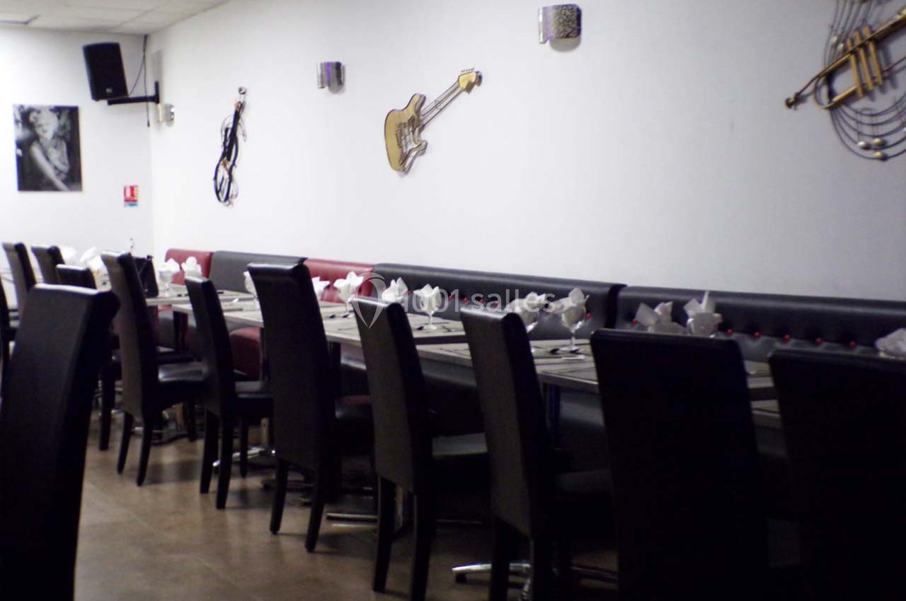 Salle de restaurant avec une longue table dressée, entourée de chaises noires, et décorations murales en forme d'instruments…
