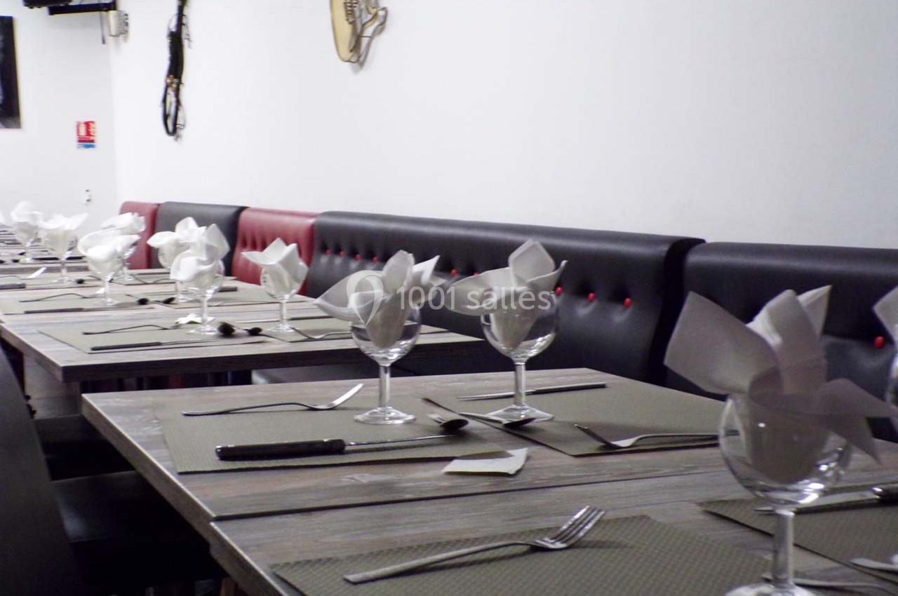 Salle de restaurant avec tables alignées, nappes grises, verres à pied et serviettes pliées en éventail.