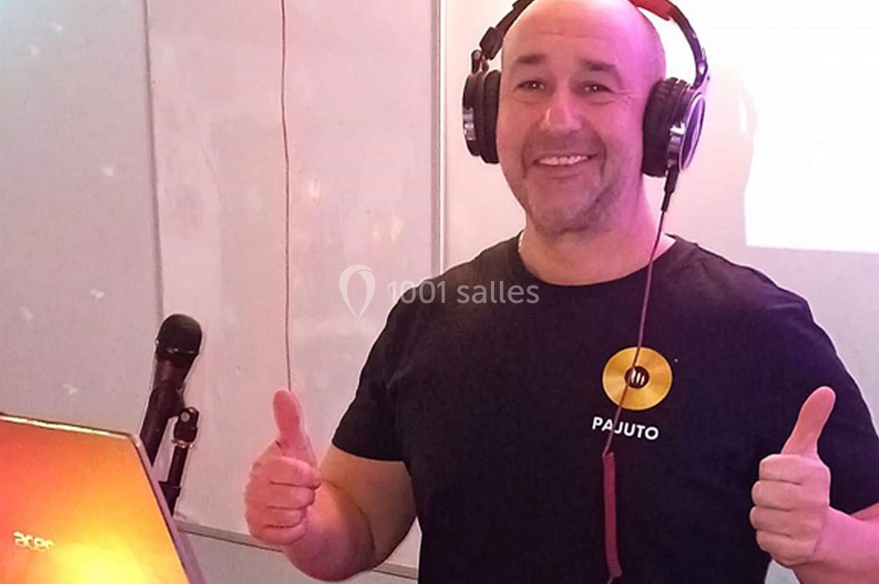 Un homme souriant portant un casque audio lève les pouces devant un ordinateur portable et un micro.