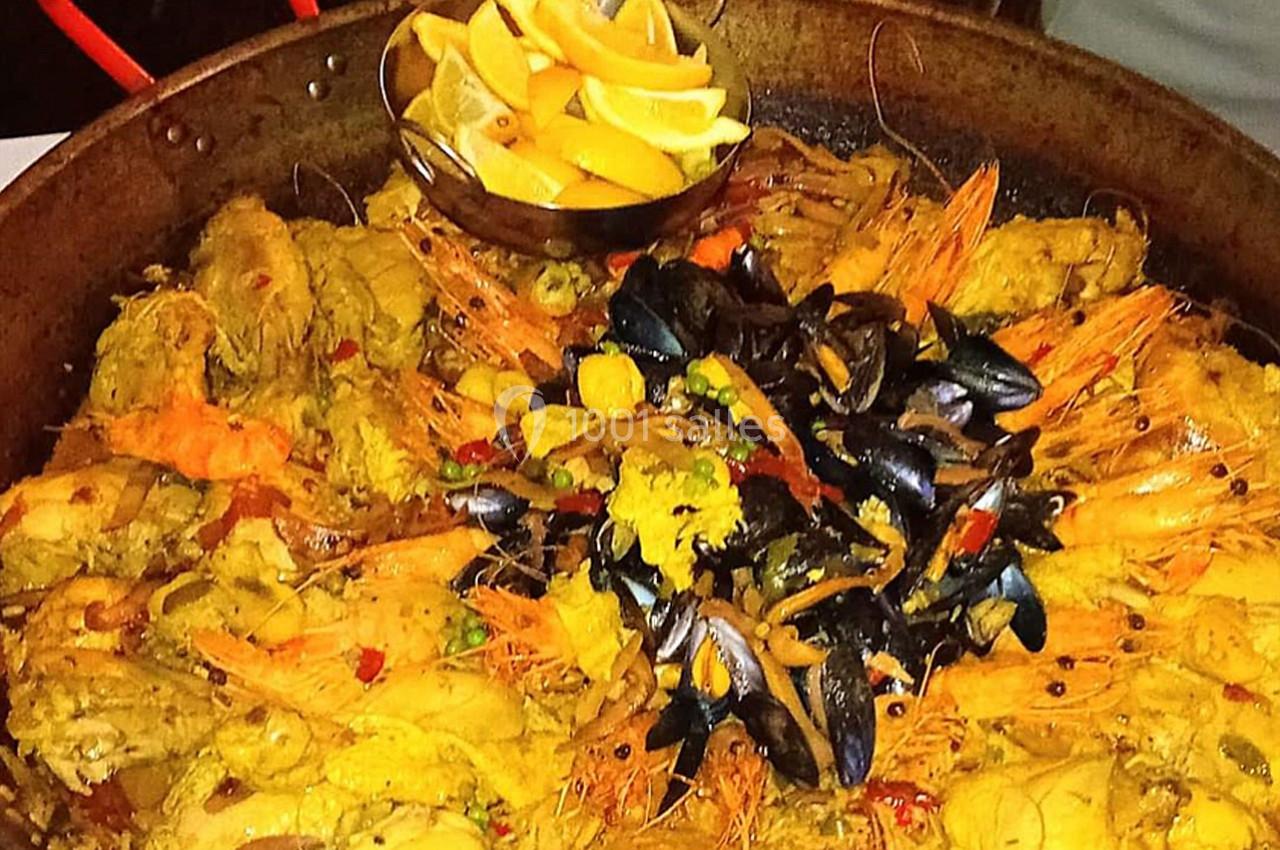 Plat de paella aux fruits de mer avec crevettes, moules, morceaux de poulet et citron en garniture.