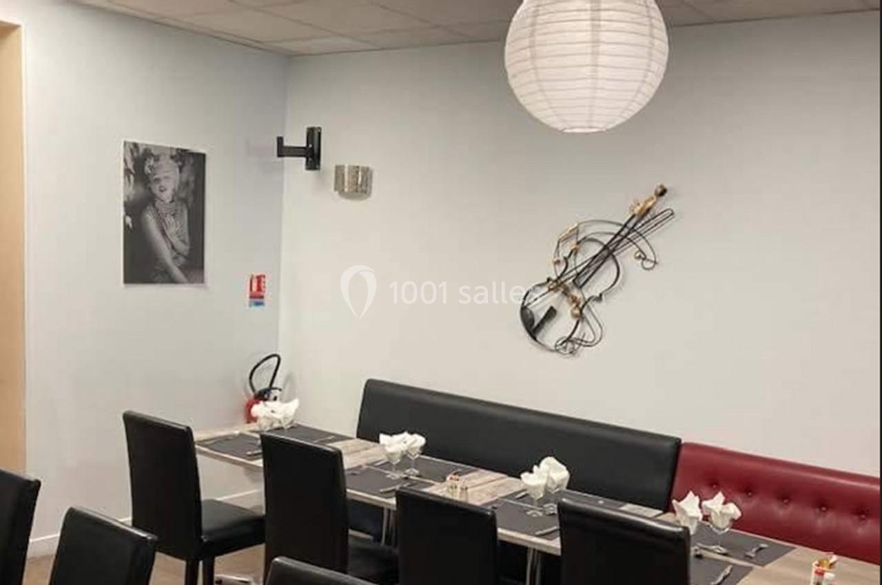 Salle de restaurant avec table dressée, chaises noires, décoration murale en forme de violon et lampe suspendue.