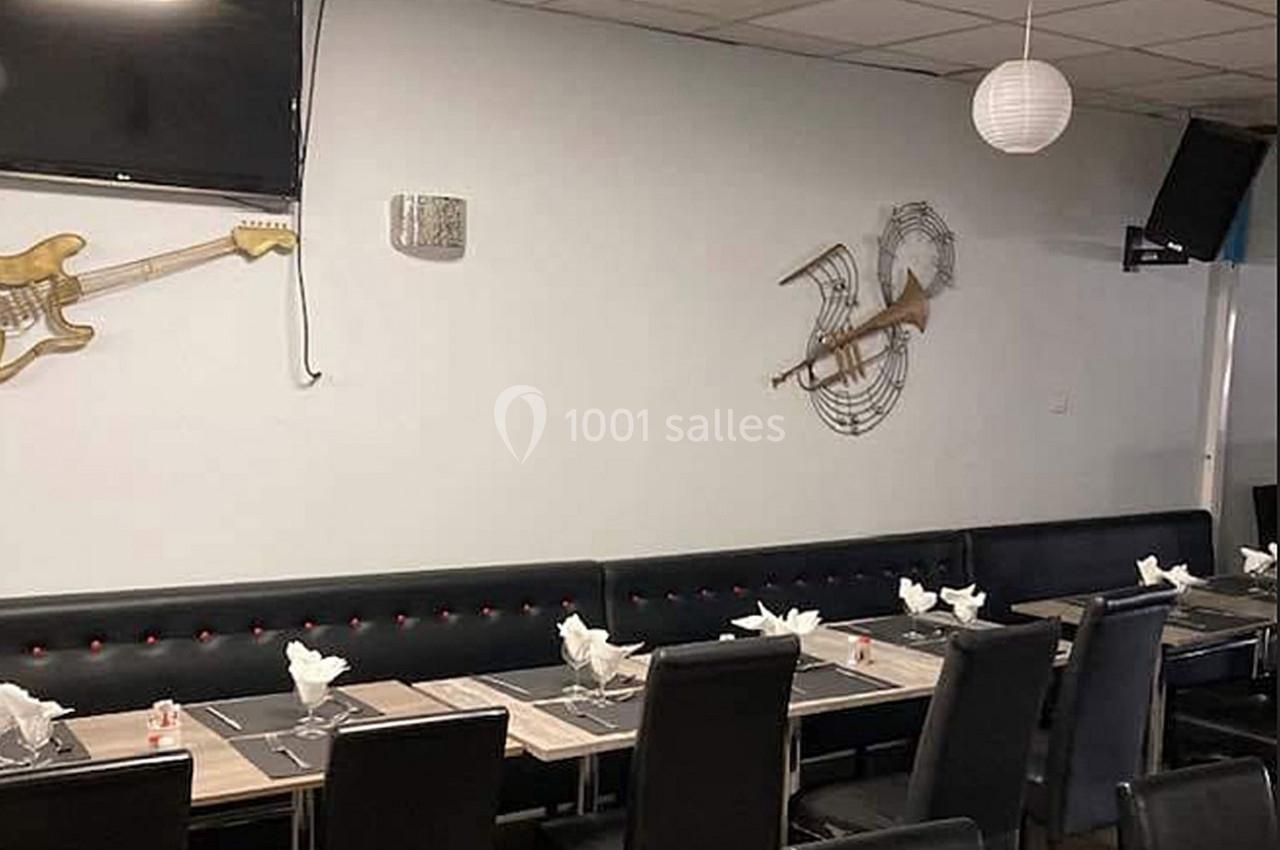 Salle de restaurant avec tables dressées, chaises noires et décorations murales en forme de guitares.