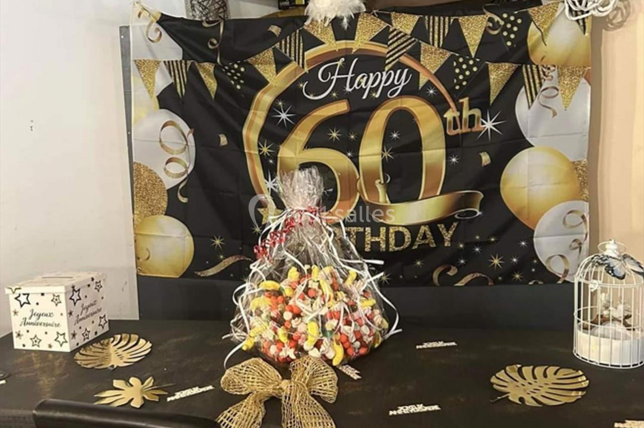 Décoration d'anniversaire pour un 60e anniversaire avec banderoles dorées, ballons et un panier de bonbons sur une table.