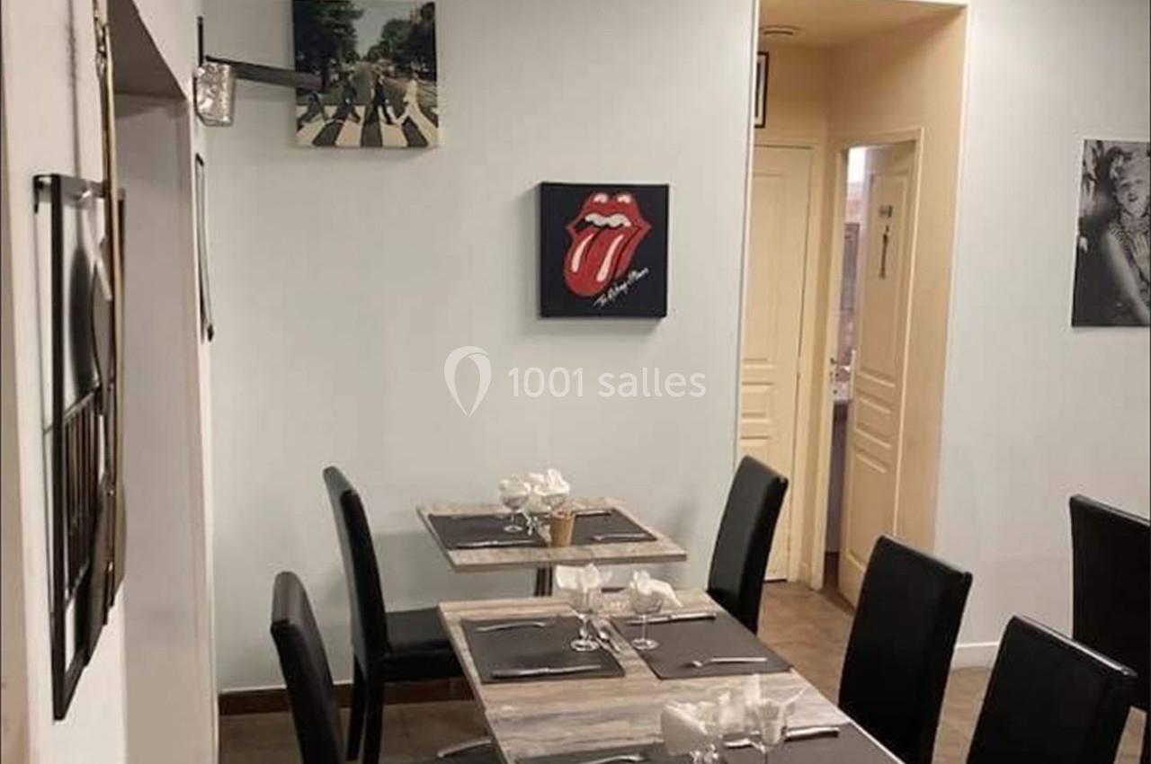 Salle de restaurant avec tables dressées, chaises noires et décorations murales, dont une affiche des Rolling Stones.