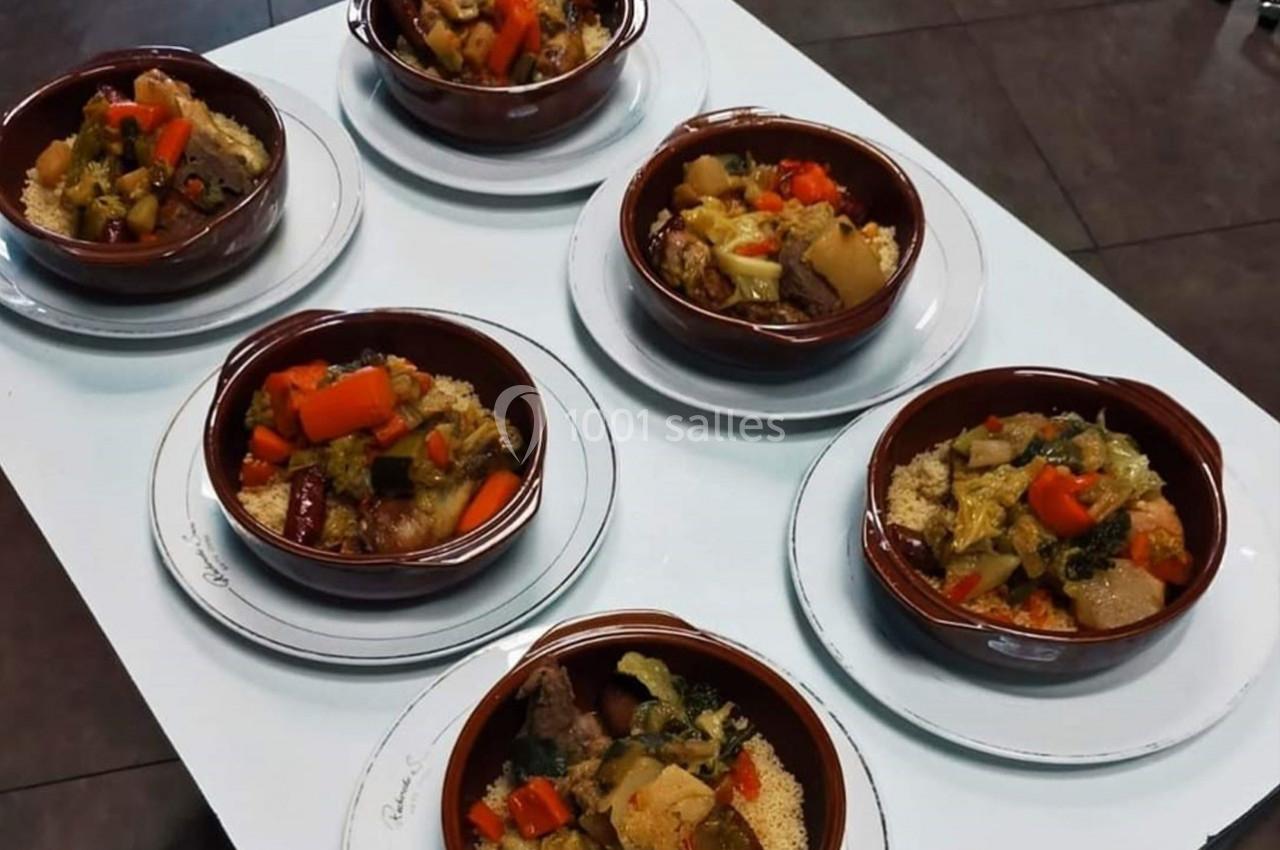 Six assiettes de couscous garnies de légumes variés et de viande, disposées sur une table blanche.