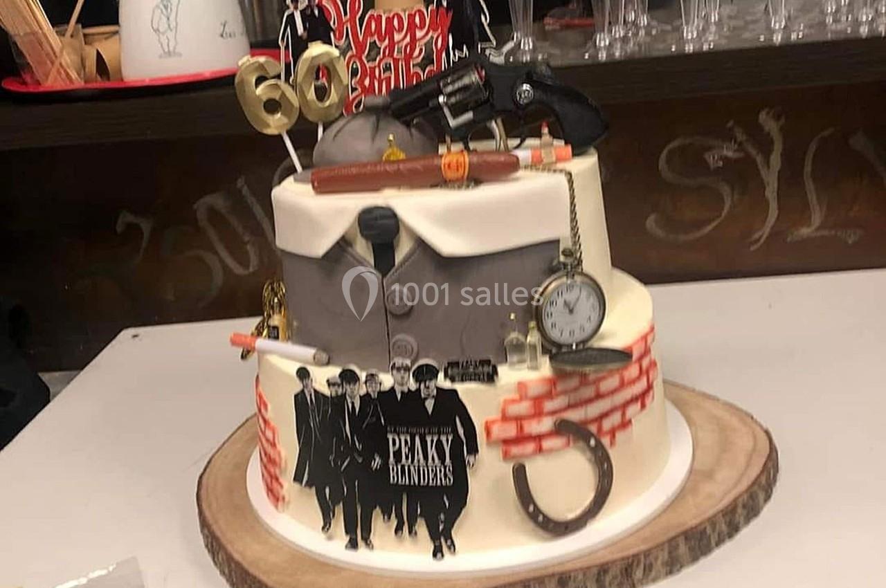 Gâteau d'anniversaire décoré sur le thème de ’Peaky Blinders’ avec des accessoires et une inscription ’60’.
