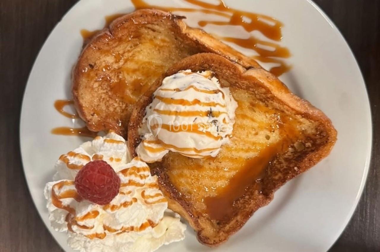 Deux tranches de pain perdu avec glace vanille, chantilly, caramel et une framboise, servies sur une assiette blanche.