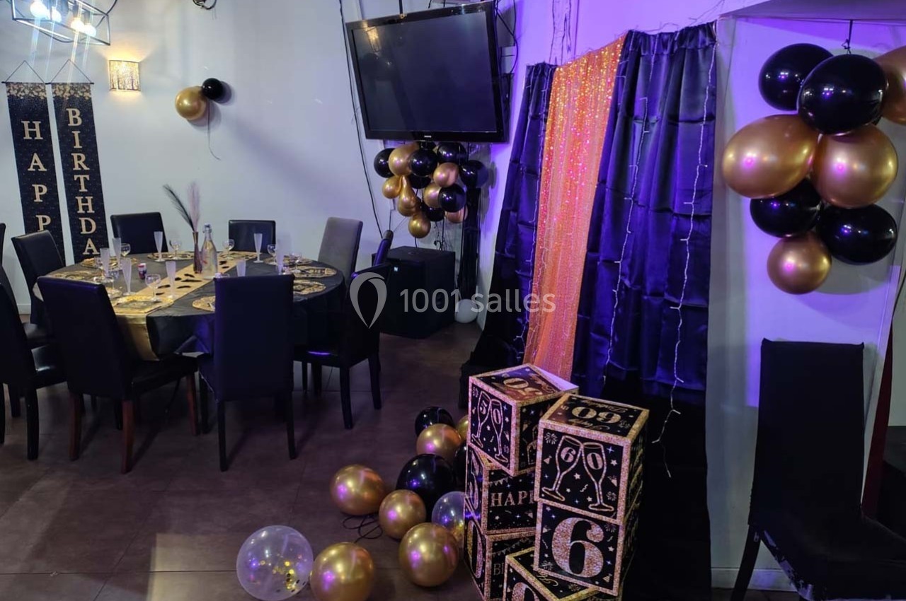 Salle décorée pour un anniversaire avec ballons noirs et dorés, table dressée et cubes affichant le chiffre 6.