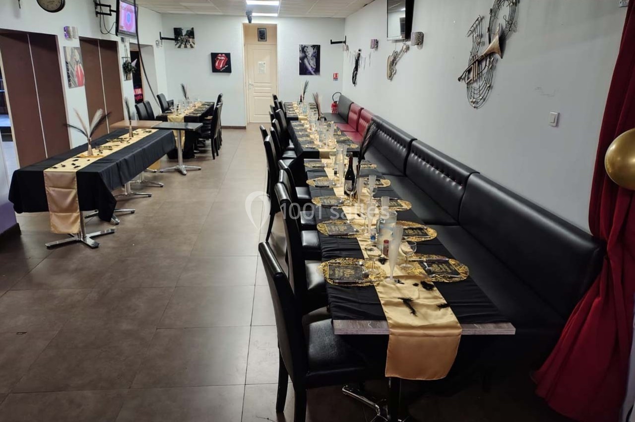 Salle de réception avec tables alignées, nappes noires et dorées, décorations murales et ambiance sobre.