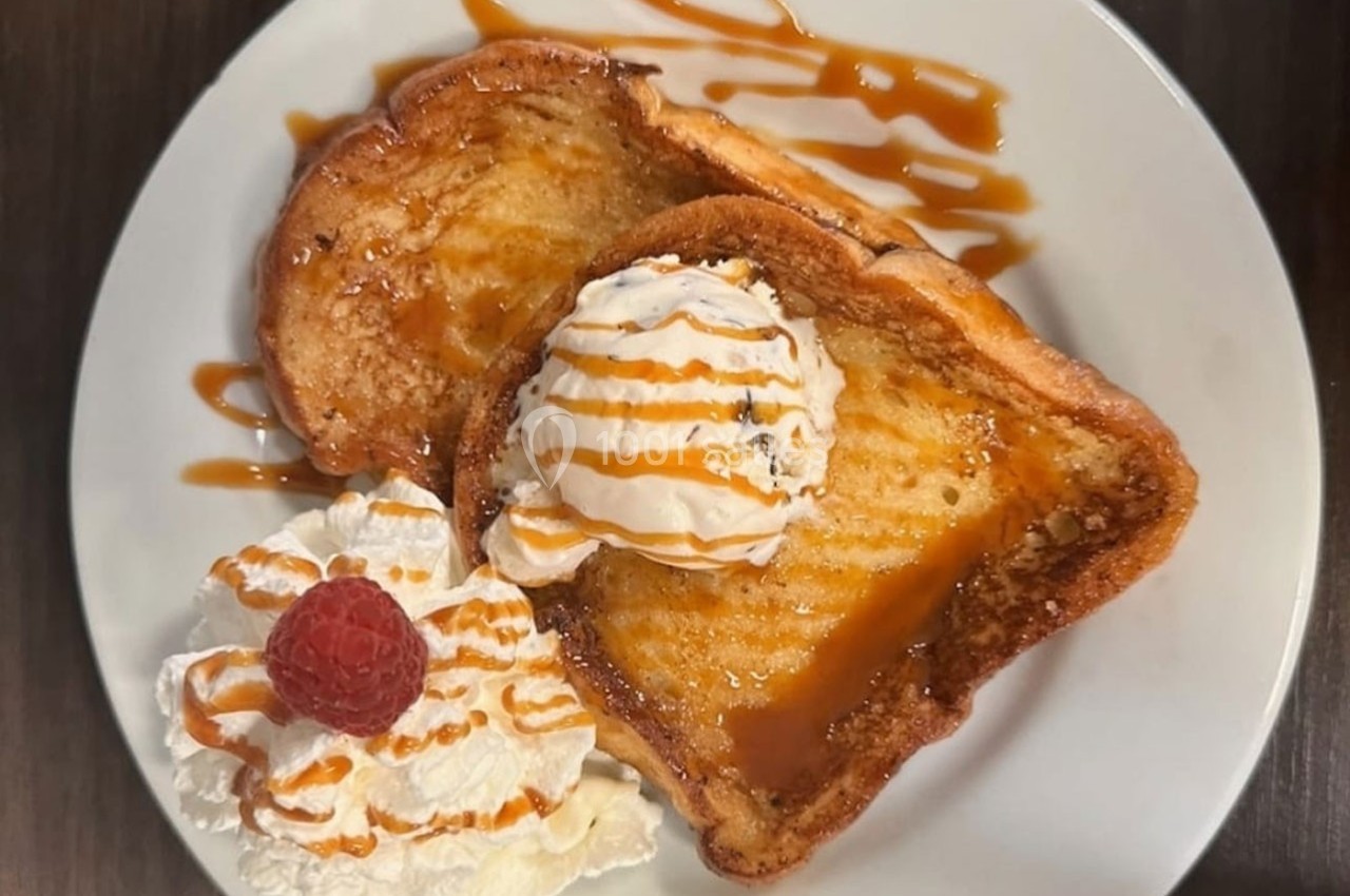 Deux tranches de pain perdu avec boule de glace, chantilly, framboise et filet de caramel sur une assiette blanche.