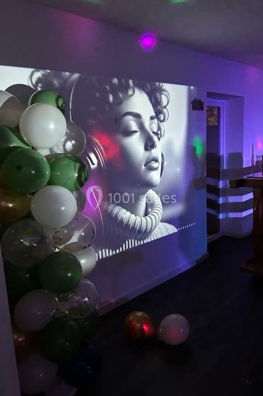 Projection en noir et blanc d'une femme avec un casque audio, entourée de ballons dans une pièce faiblement éclairée.