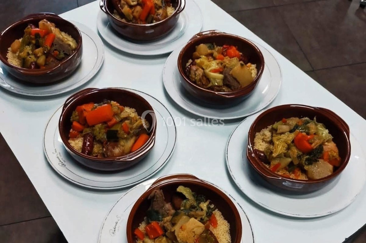 Six assiettes de couscous garnies de légumes variés et de viande, disposées sur une table blanche.