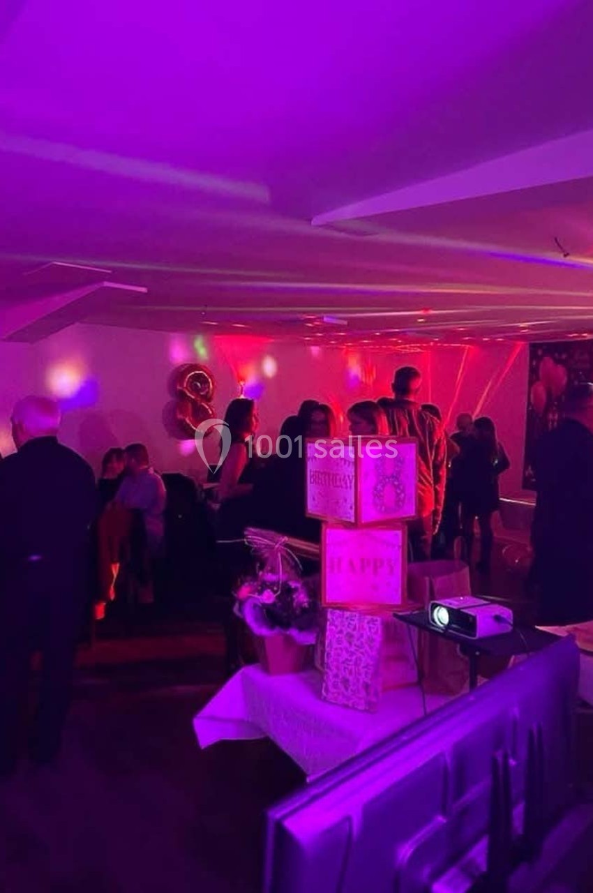 Des personnes debout et assises dans une salle décorée avec des lumières colorées, des ballons et des cadeaux.