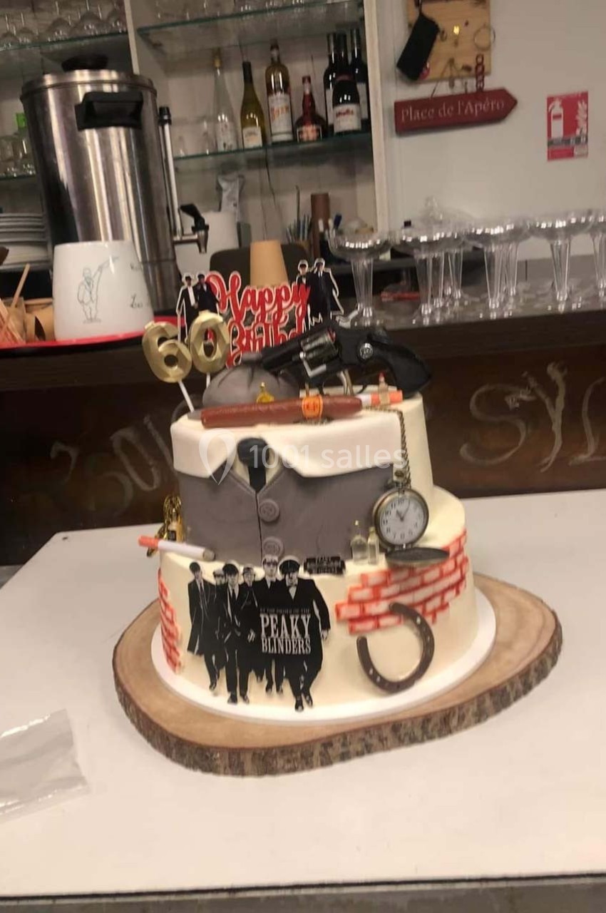 Gâteau à deux étages décoré sur le thème de la série Peaky Blinders, avec des accessoires et détails vintage.