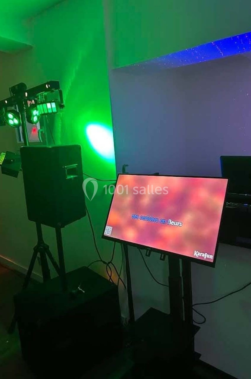 Équipement de karaoké avec écran affichant des paroles, haut-parleur et éclairage coloré dans une pièce sombre.