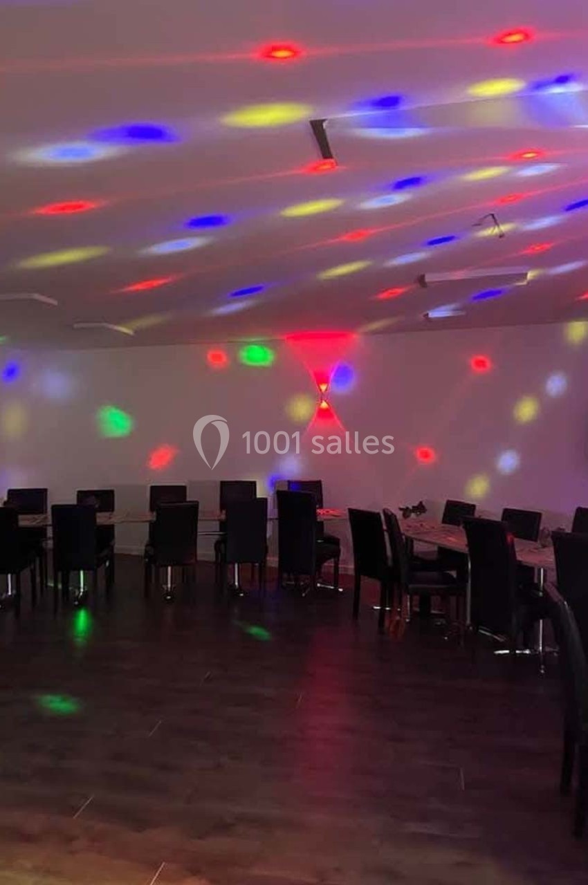 Salle sombre avec des tables et des chaises alignées, éclairée par des lumières colorées projetées au plafond.