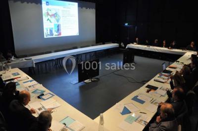 Un groupe de personnes assises observe un aquarium géant avec des poissons et des requins, guidé par une animatrice.