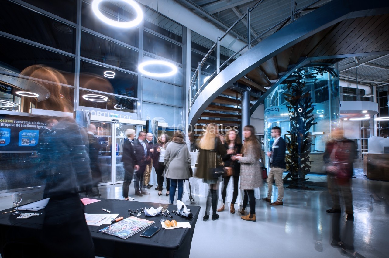 Location salle Montpellier (Hérault) - Planet Ocean Montpellier #3 Des personnes discutent dans un espace moderne avec un escalier en colimaçon et des éclairages circulaires suspendus.