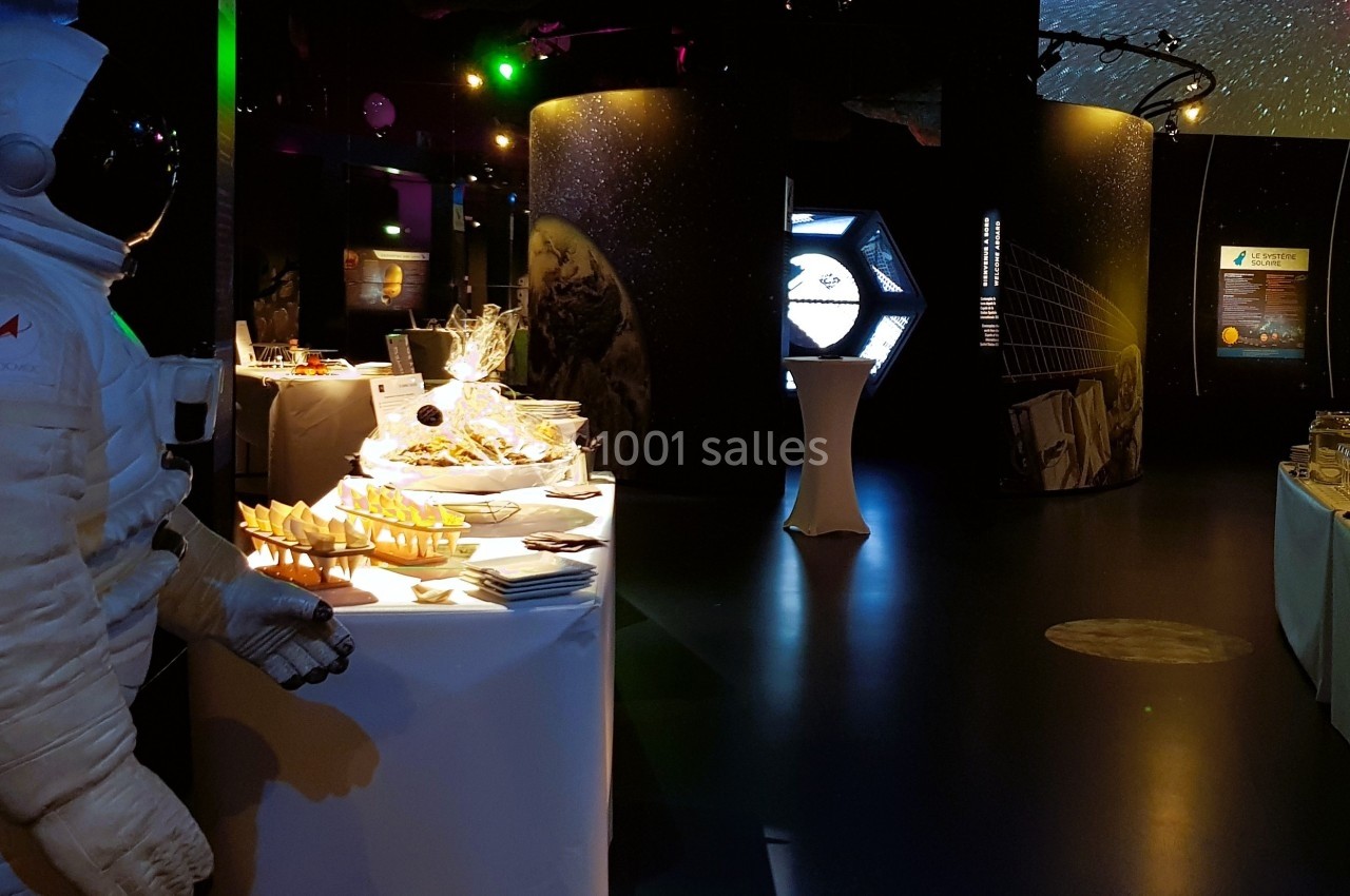 Un mannequin en combinaison d'astronaute près d'un buffet éclairé dans une salle à thème spatial.