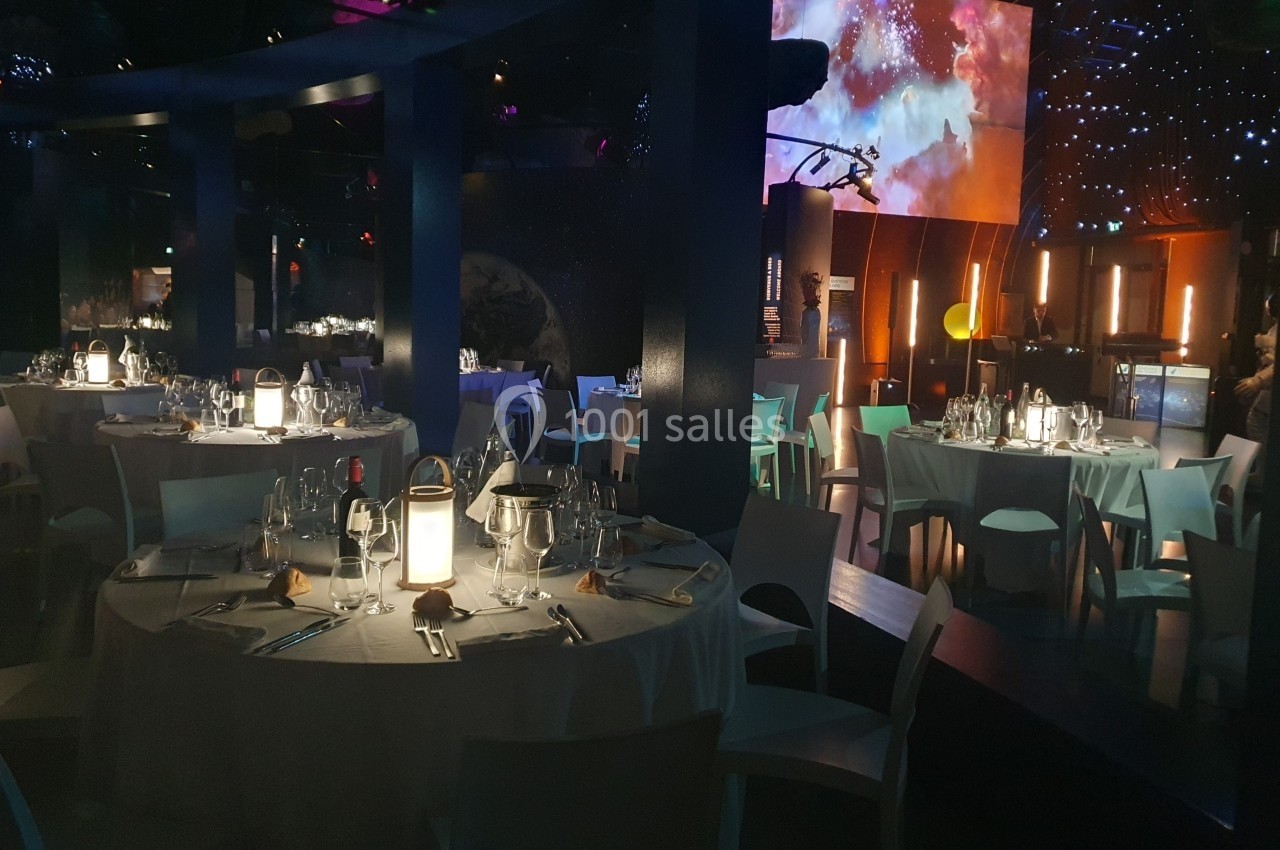 Salle de restaurant décorée avec des tables rondes dressées, éclairage tamisé et ambiance étoilée.