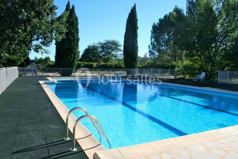 Piscine extérieure entourée de végétation, avec margelle en pierre et clôture de sécurité.