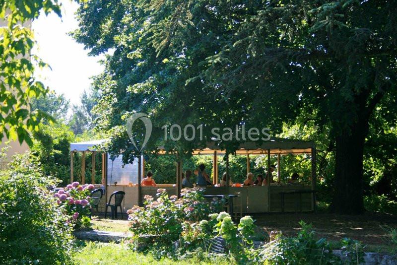 Un groupe de personnes assises sous un abri en bois dans un jardin verdoyant avec des arbres et des fleurs.