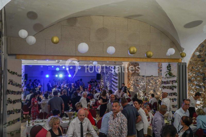 Salle décorée avec des guirlandes et lanternes, remplie d'invités assis et debout lors d'un événement festif.