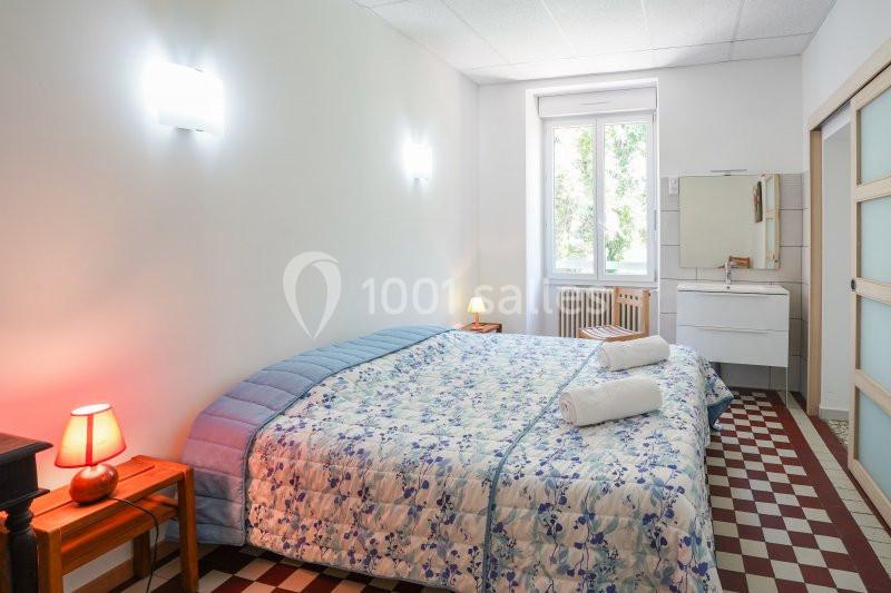 Chambre lumineuse avec lit double, couvre-lit fleuri, lampes de chevet et fenêtre donnant sur un espace arboré.