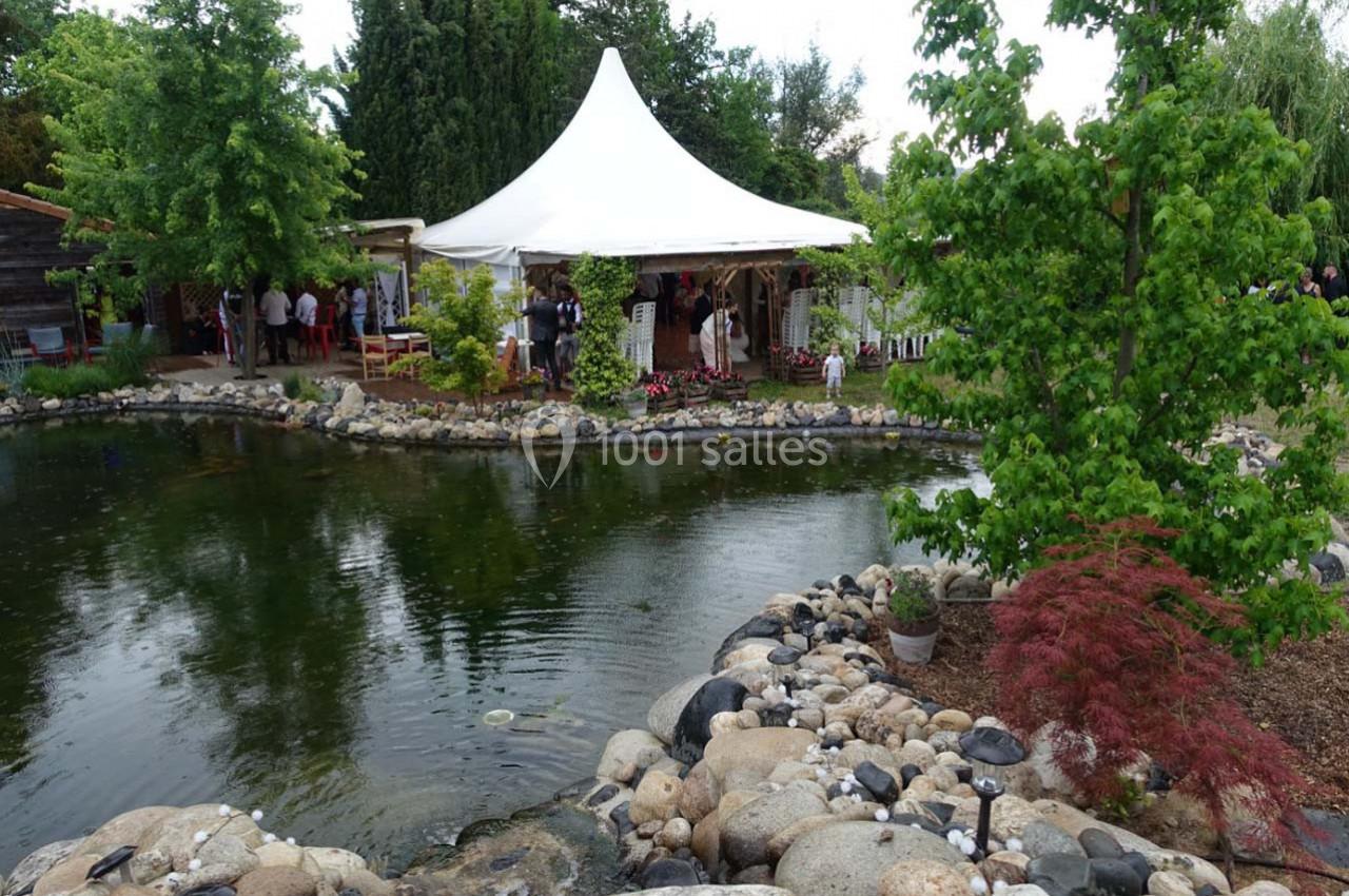 Étang entouré de rochers et de végétation, avec une tente blanche et des personnes rassemblées en arrière-plan.