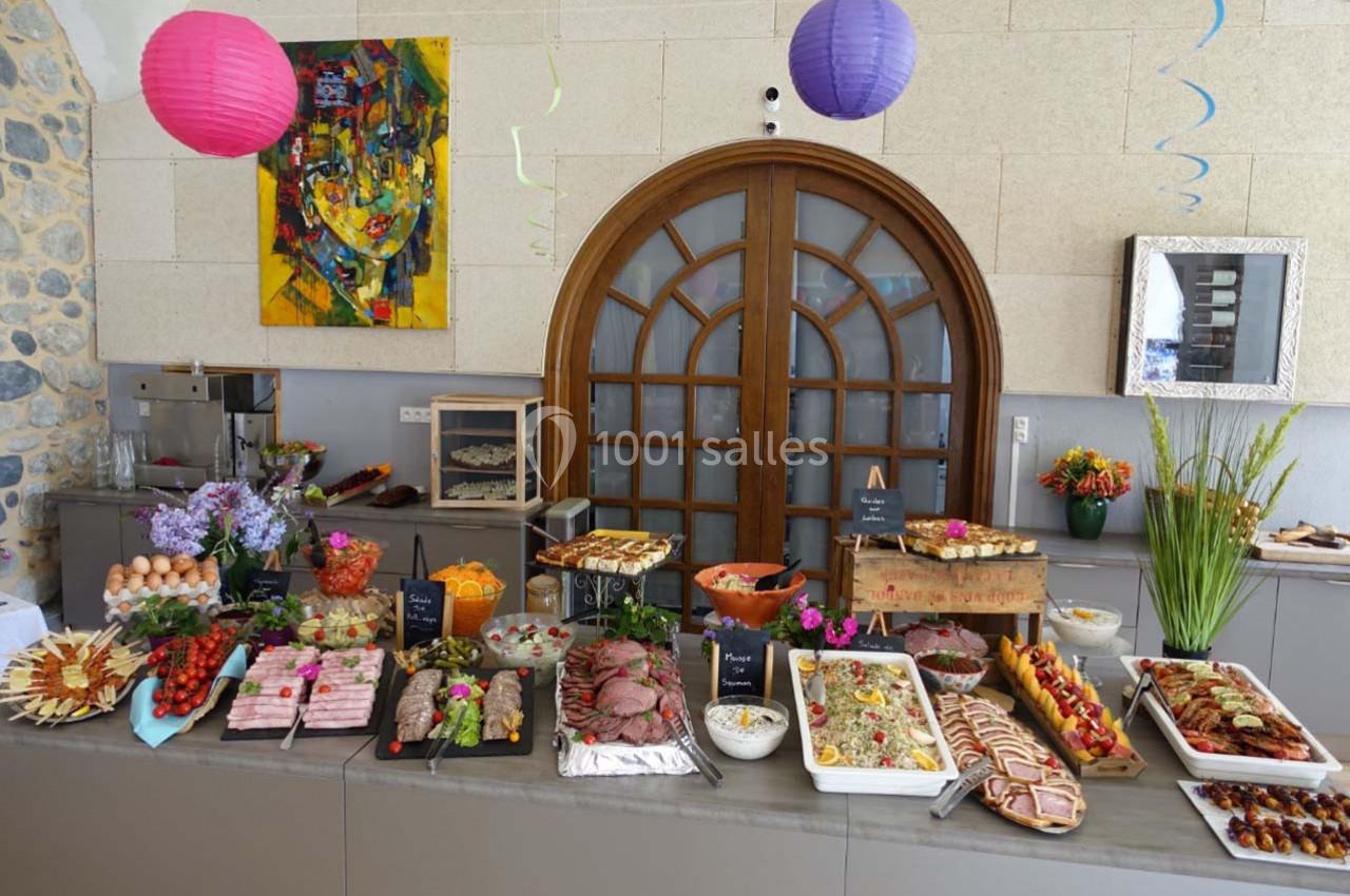 Buffet varié avec plats froids, charcuterie, légumes, desserts et décorations colorées dans une salle lumineuse.