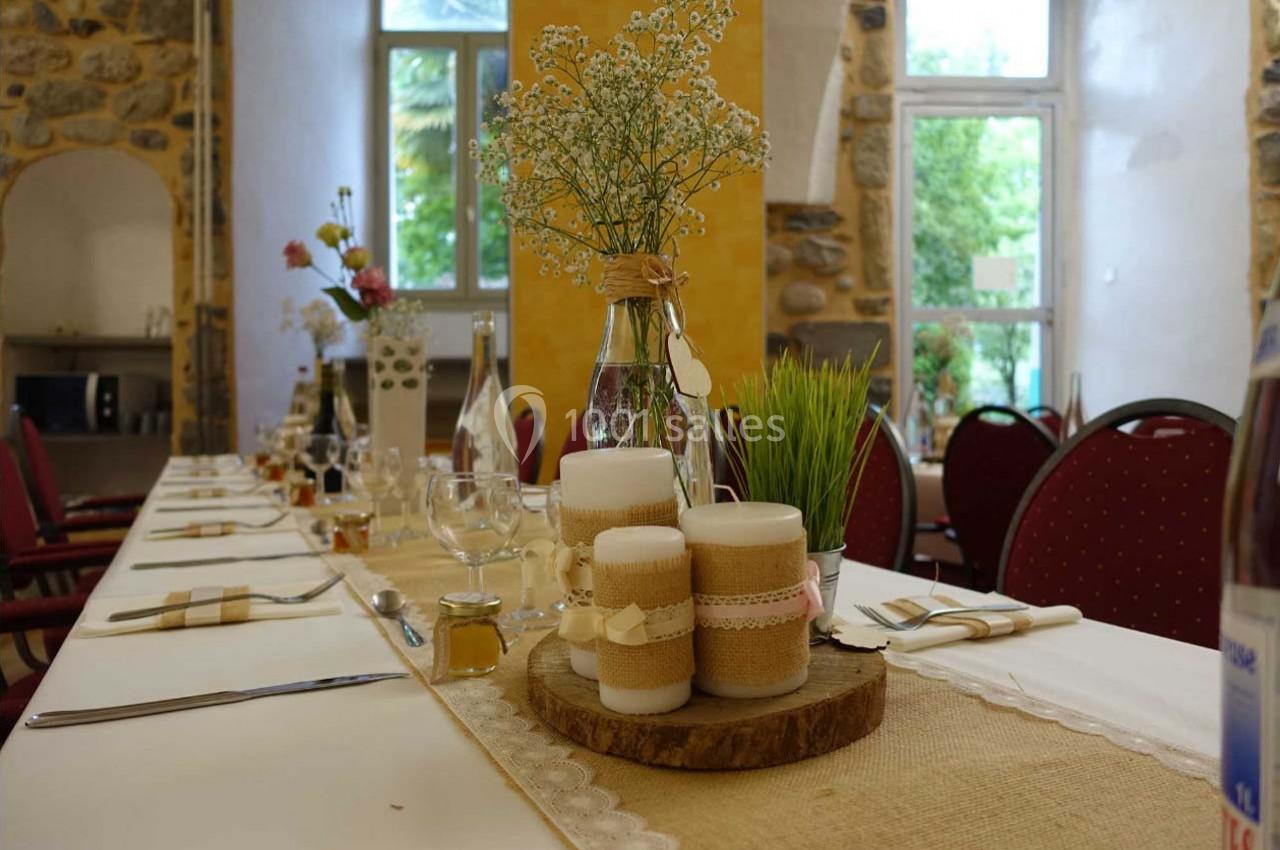 Table décorée pour un repas avec bougies, fleurs et éléments rustiques, dans une salle lumineuse aux murs en pierre.