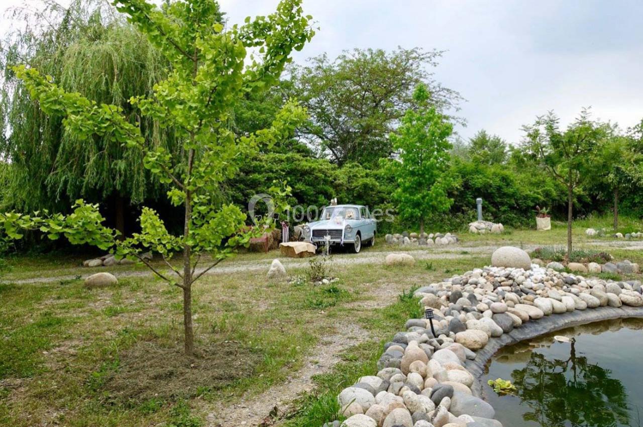 Une voiture ancienne stationnée dans un jardin verdoyant près d'un étang entouré de pierres.