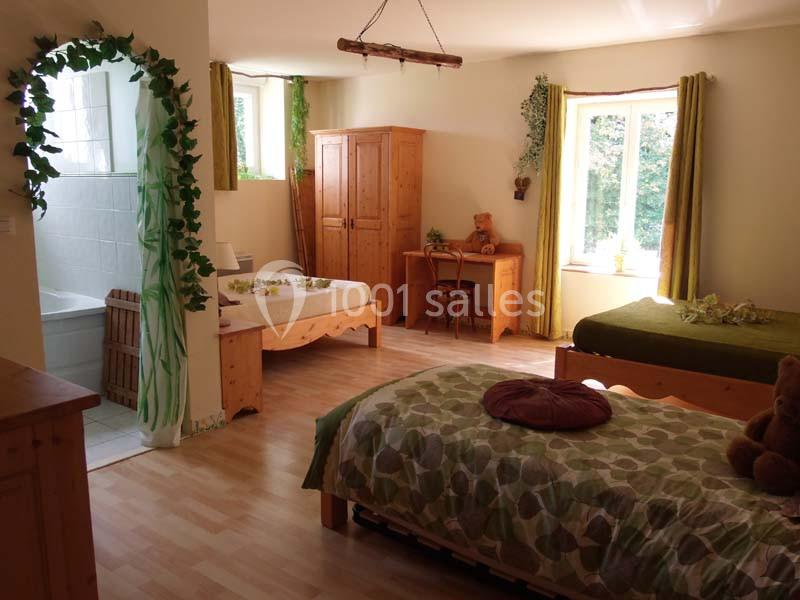 Chambre lumineuse avec trois lits en bois, un bureau, une armoire, des plantes décoratives et une salle de bain attenante.