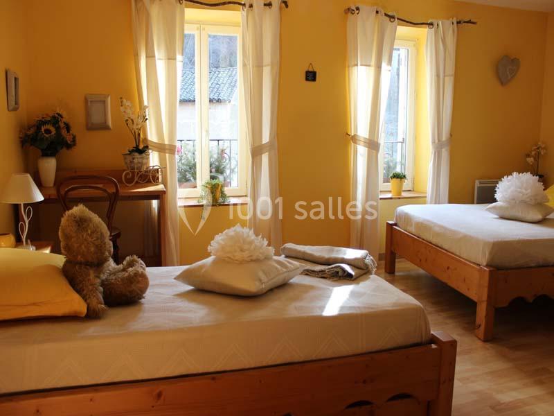 Chambre lumineuse avec murs jaunes, deux lits simples, décorations florales et une peluche sur un lit.