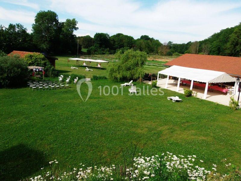 Grand espace vert avec pelouse, chaises disposées en extérieur, tonnelle blanche et bâtiments aux toits rouges.