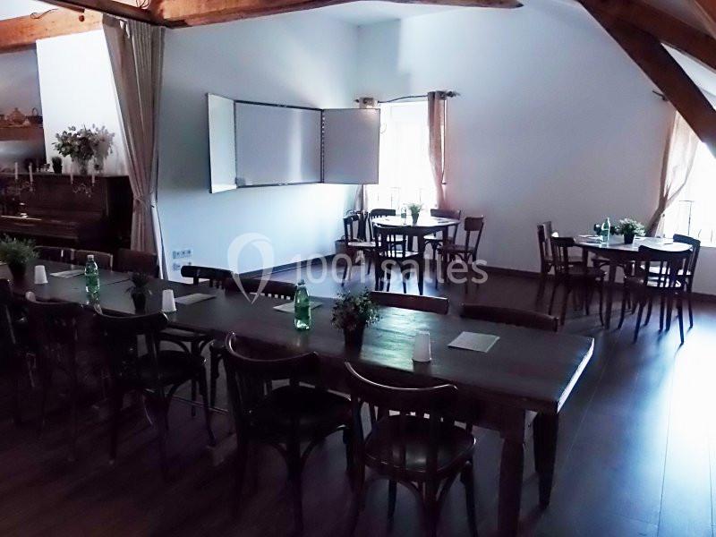 Salle lumineuse avec des tables en bois, des chaises, un tableau blanc et des bouteilles d'eau disposées pour une réunion.