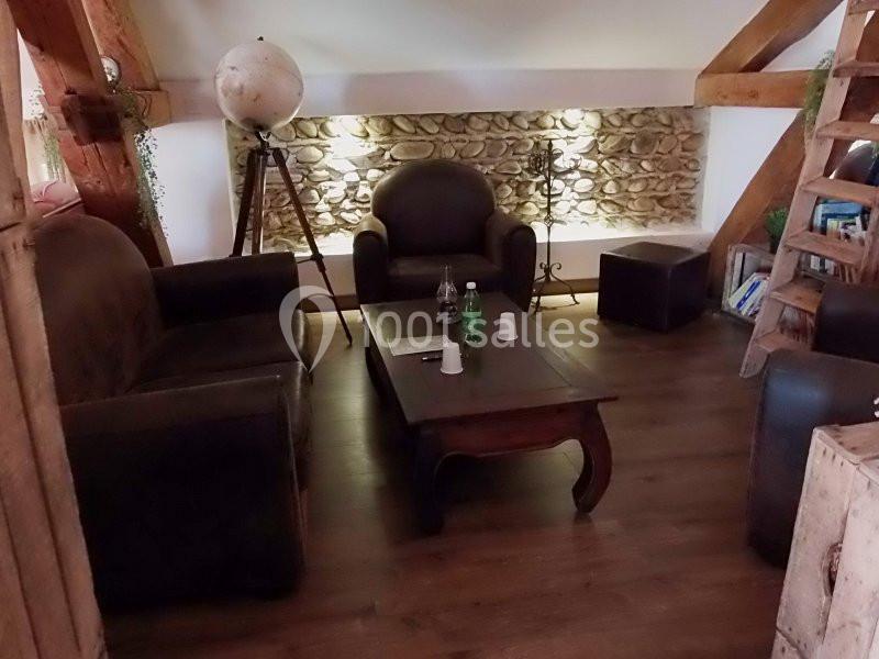 Salon cosy avec fauteuils en cuir, table basse en bois, globe terrestre et mur en pierre éclairé.