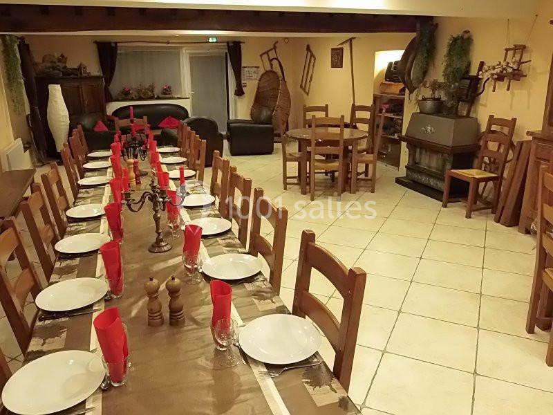 Grande salle à manger rustique avec une longue table dressée, entourée de chaises en bois, décorée de serviettes rouges.