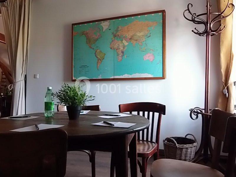 Table ronde en bois entourée de chaises, avec des documents, une bouteille et une plante, devant une carte du monde au mur.