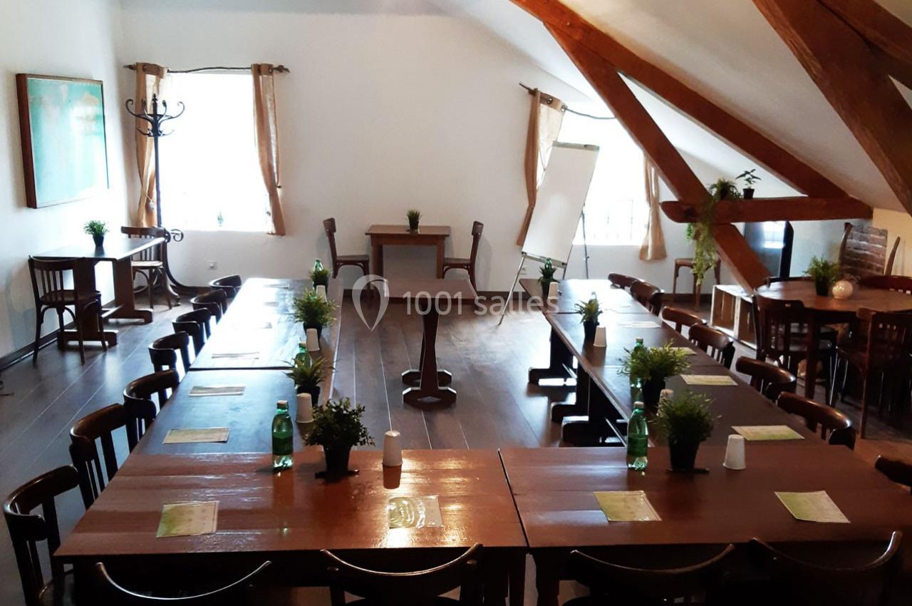 Salle de réunion lumineuse avec tables en bois disposées en U, chaises, plantes décoratives et un tableau de présentation.