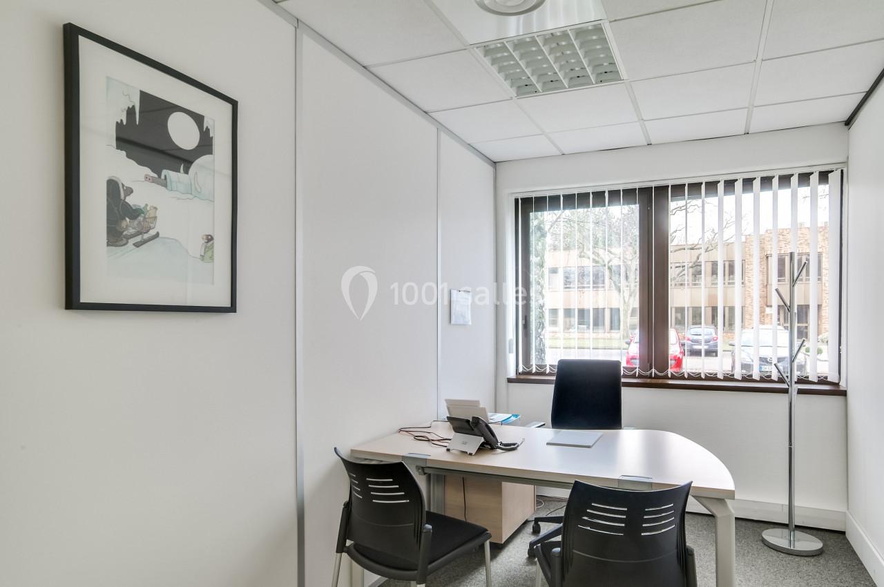 Bureau lumineux avec un bureau blanc, trois chaises, un téléphone, une fenêtre avec stores et un tableau au mur.