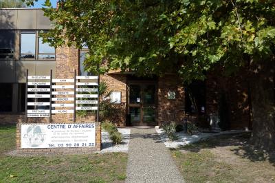 Façade d'un centre d'affaires en briques, avec une entrée bordée de végétation et des panneaux d'information.