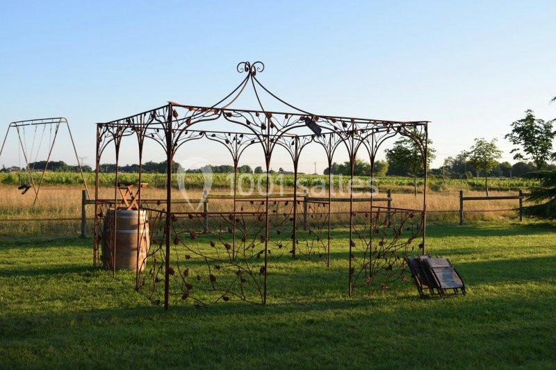Structure métallique décorative dans un jardin, entourée de pelouse et de champs avec un ciel dégagé en arrière-plan.