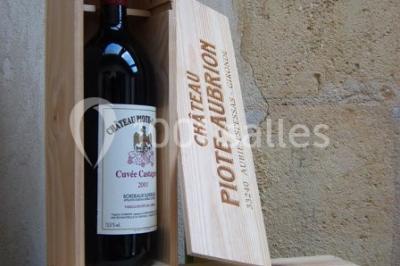 Bouteille de vin rouge dans une caisse en bois ouverte, posée contre un mur en pierre.