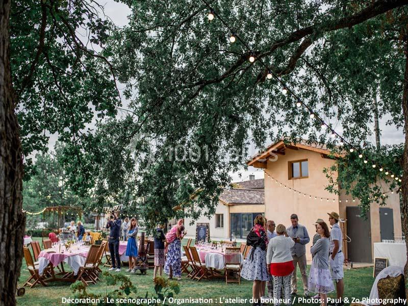 Groupe de personnes discutant dans un jardin décoré avec des guirlandes lumineuses, tables et chaises en bois.